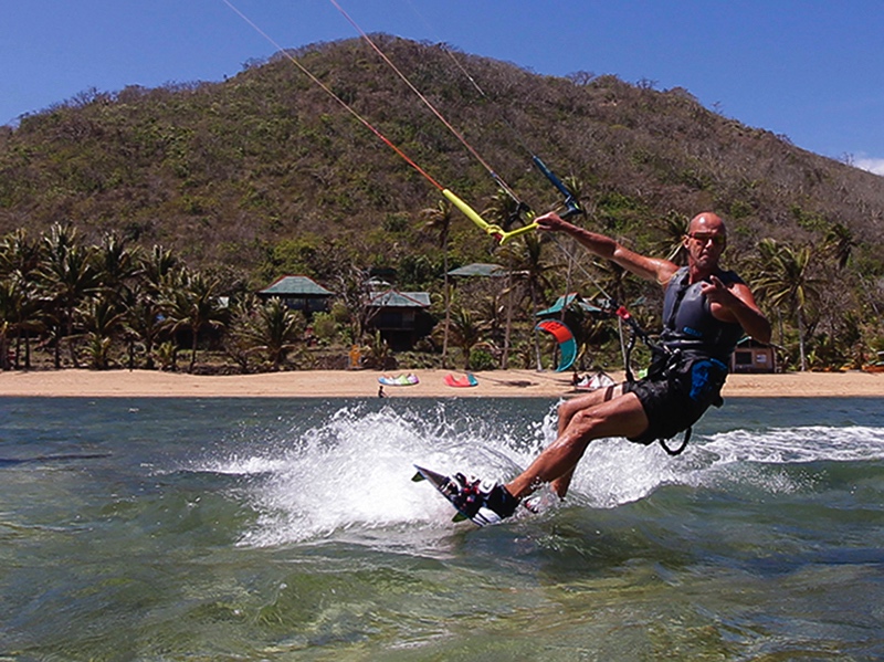 Man kiteboarding in the sea near a tropical island with a mountain in the background.